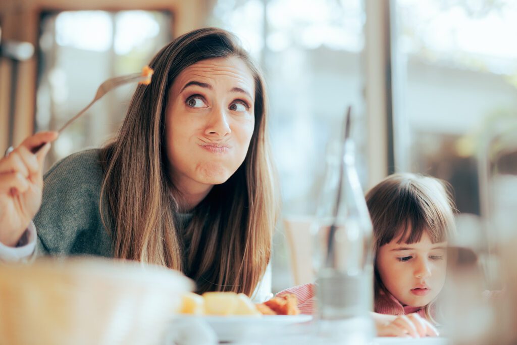 mother making a frustrated face holding a fork with nutritious food her young daughter won't eat picky eater