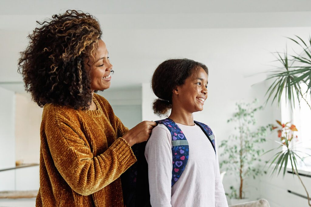 black mother and daughter getting ready for school in the morning putting on backpack smiling