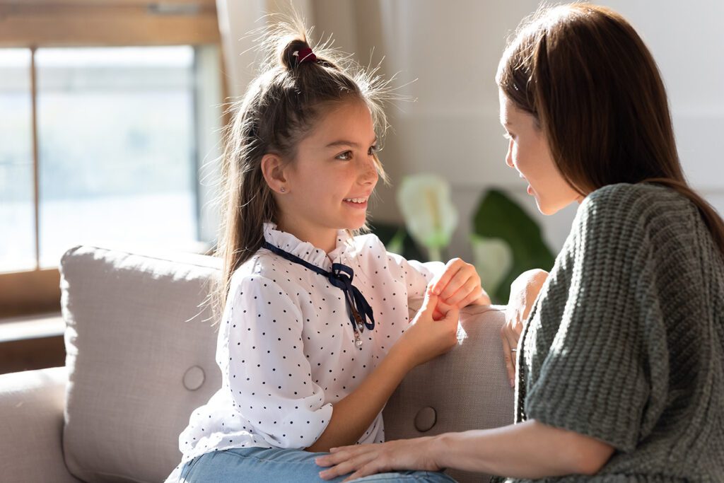 mother and young daughter talking on a coach in their living room